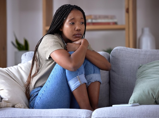 Sad depression and lonely black woman on sofa with mental health issue problems and stress Thinking reflection and depressed girl sitting in living room with mistake failure and negative emotion