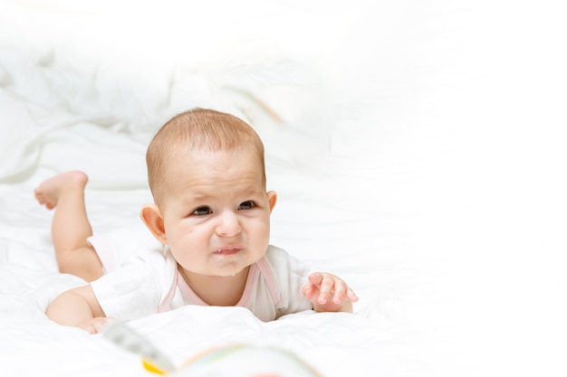 Sad and disappointed baby girl is lying on bed Infant child on her stomach Drooling and teething