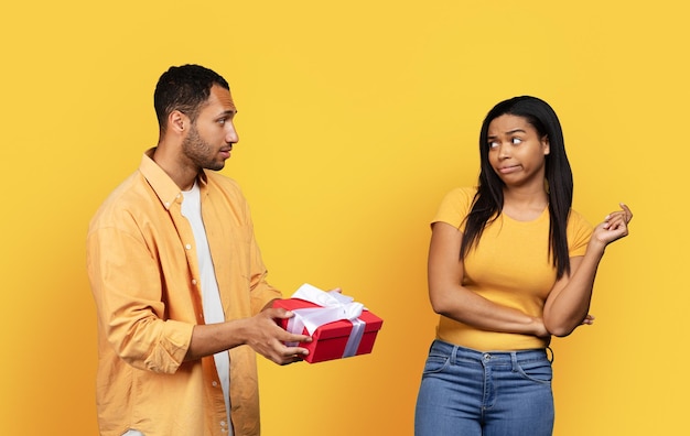 Sad disappointed millennial african american guy giving box to displeased woman