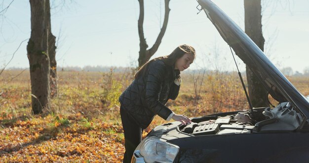 壊れた車で悲しい失望した女性。欲求不満の女性が自動車事故を修理します。車両チェックエンジンの損傷トラブル。コンセプト交通事故。