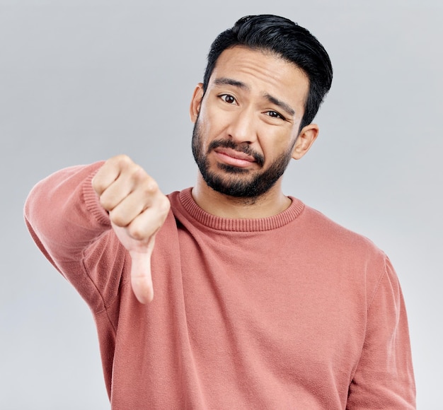 Sad disappointment and portrait of an Asian man with a thumbs down isolated on a studio background Review unhappy and a Chinese guy with a hand sign for a problem mistake and dislike emoji