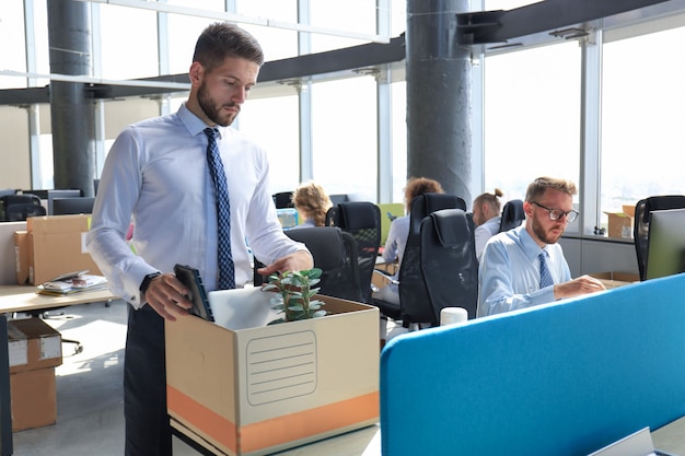 Sad dismissed worker are taking his office supplies with him from office.