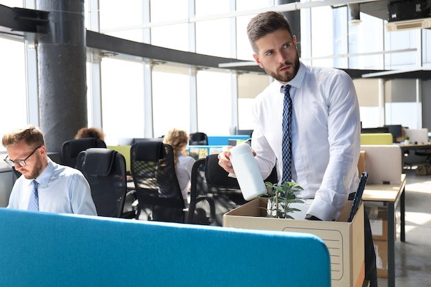 Sad dismissed worker are taking his office supplies with him from office.