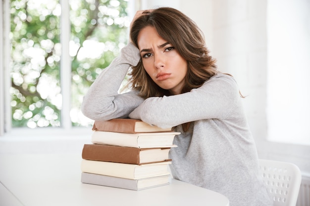 Sad displeased tired young lady on a lot of books.