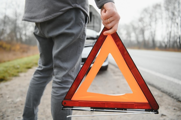 道路上の壊れた車の近くに立ってエンジンの問題を抱えている悲しいドライバー車の故障の概念