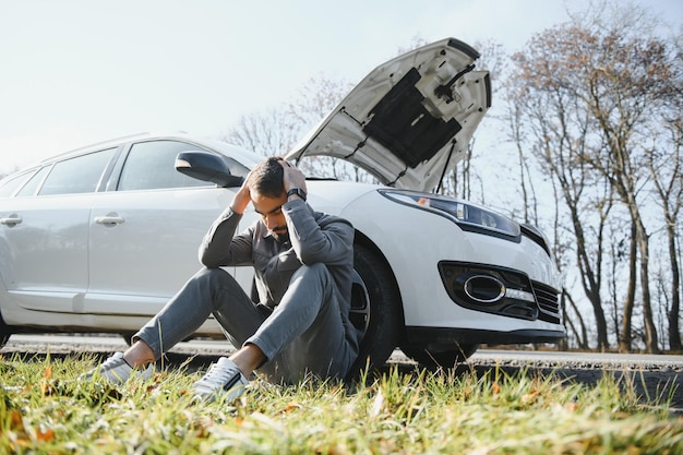 Sad driver holding his head having engine problem standing near broken car on the road Car breakdown concept