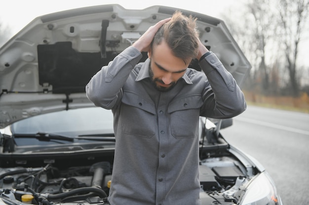 Sad driver holding his head having engine problem standing near broken car on the road Car breakdown concept