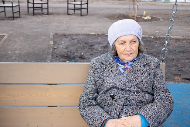 грустная пожилая женщина отдыхает на качелях на открытом воздухе весной крупным планом