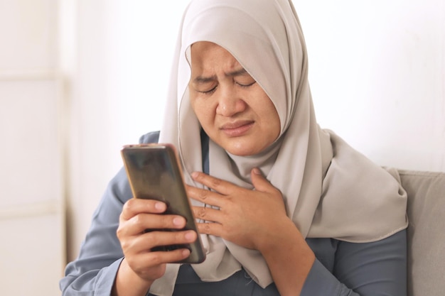 슬픈 감정적 인 아시아 무슬림 여성 이 울고 휴대 전화 로 메시지 를 보내고 전화 로 나쁜 소식