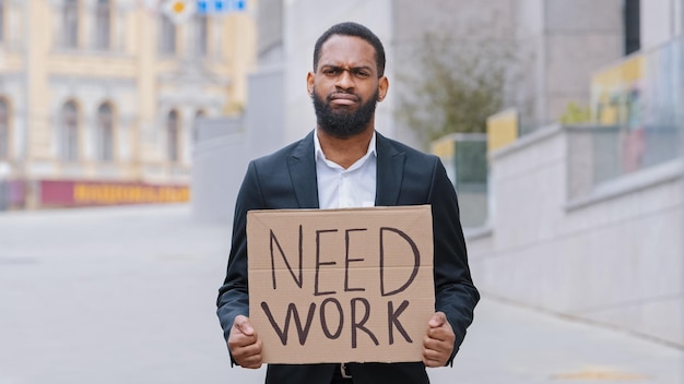 Triste frustrato senza speranza licenziato afroamericano uomo etnico sconvolto ragazzo lavoratore in città tenendo poster bisogno di lavoro aiuto ricerca lavoro offerta crisi senza lavoro disoccupazione affari persi bancarotta perdere carriera