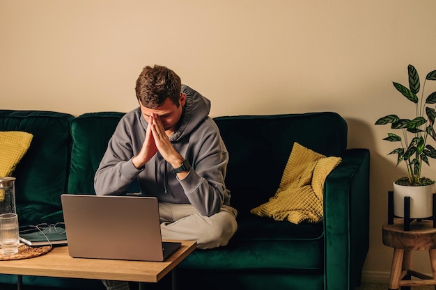 sad frustrated man sitting on the green couch in front of his laptop working overtime burnout