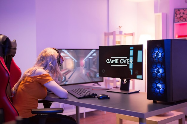 彼女はコンピューターでオンラインゲームをプレイ中に負けたので悲しい女の子。ゲーミングチェアに座っている女の子。ゲームオーバー。