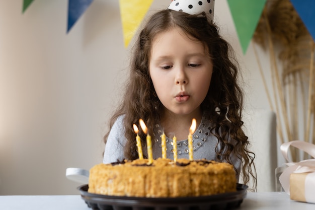 Грустная девушка задувает свечи на праздничном торте.