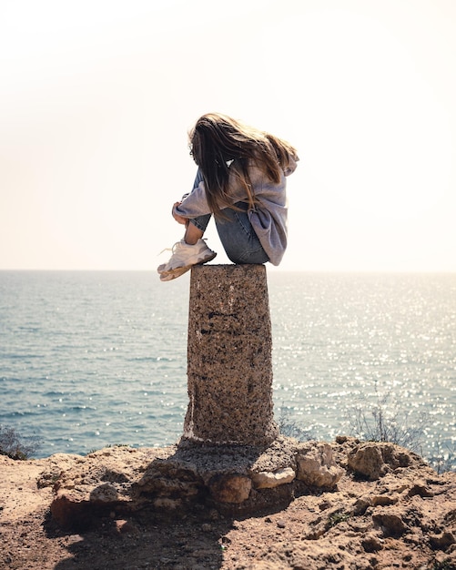 sad girl crying sitting in front of the sea in a ravine