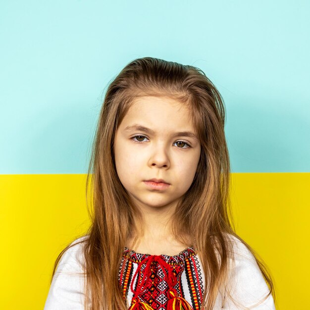 A sad girl in an embroidered shirt on the background of the ukrainian flag