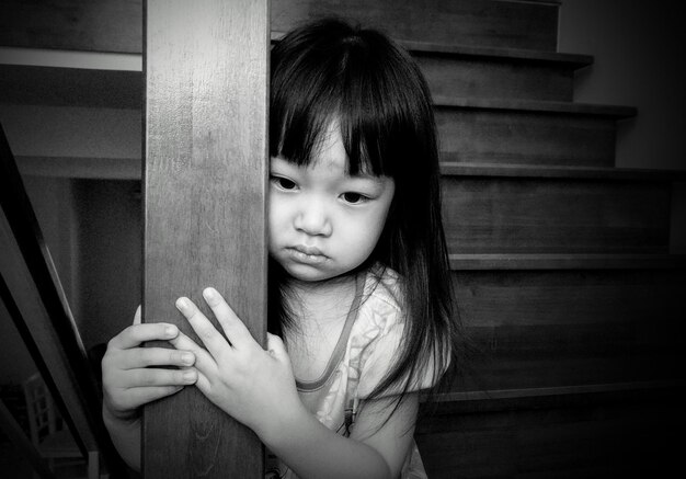 Photo sad girl holding pole while standing by steps at home