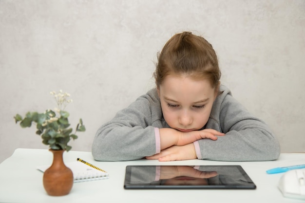 Photo sad girl sitting at the table with her head on her hands in front of the tablet with her reflection back to school
