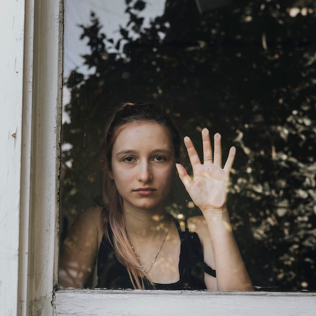 Sad girl staring out the window during a lockdown.