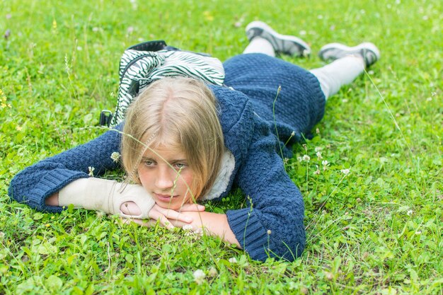 Sad girl teenager with a broken hand lies on the grass