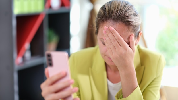 Грустная девушка расстроена чтением плохих новостей в мобильном сообщении на смартфоне в офисе за столом