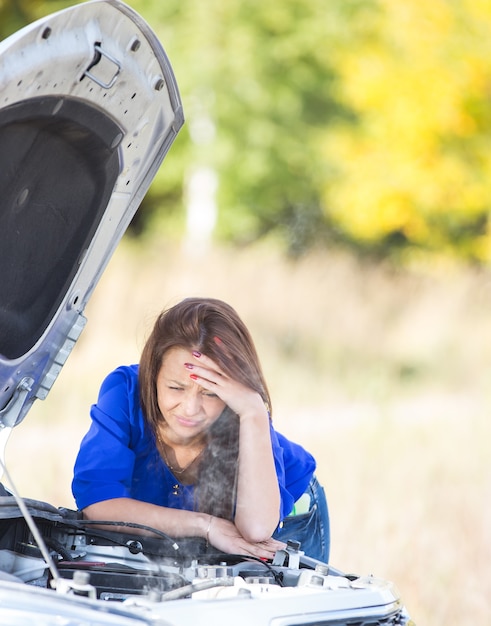 Ragazza triste con un'auto rotta con il cofano aperto