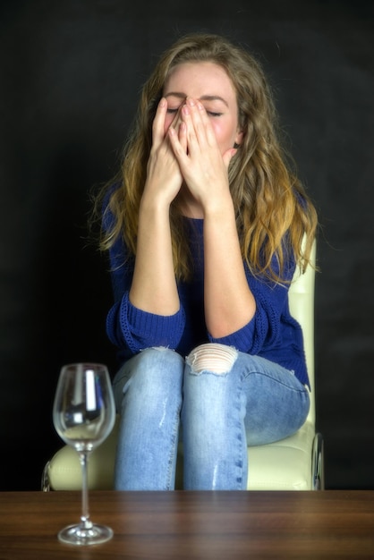 Sad girl with head in hands sitting on chair with glass of wine