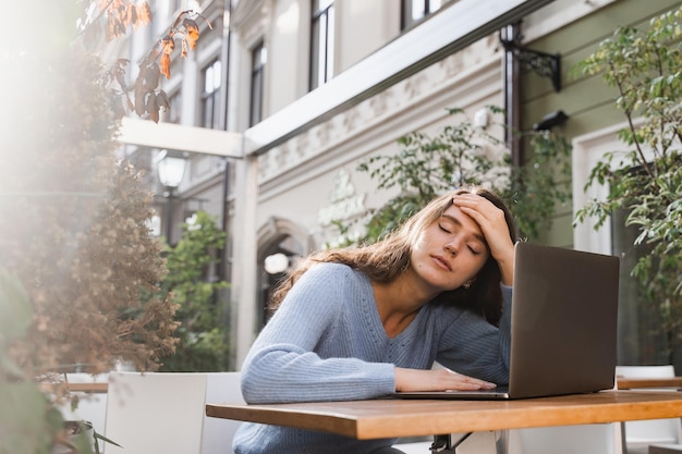 Sad girl with laptop got migraine touches her head because of pain Woman manager with strong headache working on laptop online remotely outdoor in cafe