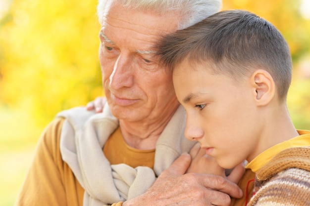 sad grandfather and grandson hugging and posing in autumn park