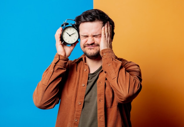 Sad guy in shirt hold alarm clock on yellow and blue backgrounds