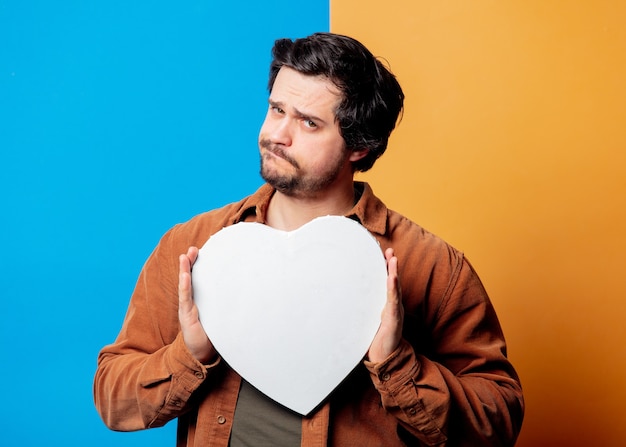 Sad guy in shirt hold heart shape banner on yellow and blue background