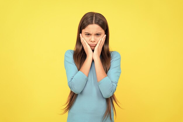 Sad kid with long hair on yellow background negative emotions