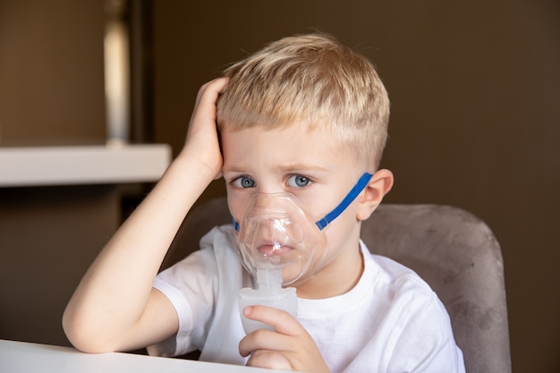 A sad little boy does inhalations with a nebulizer at home he is sick asthma Concept health