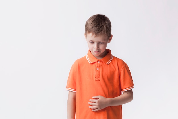 Sad little boy standing near white wall having stomach pain