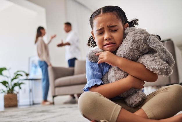 Sad little girl and crying from parent fight argument or divorce hugging teddy at home Unhappy young child in depression stress and anxiety from mother and father fighting in family disagreement