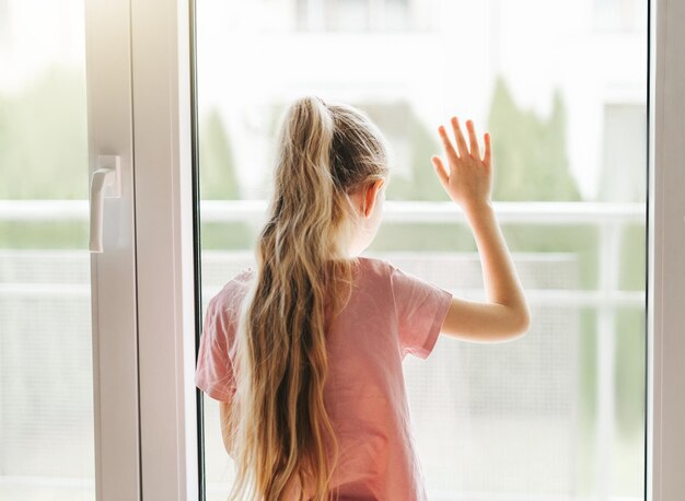 Photo sad little girl looking through window at home