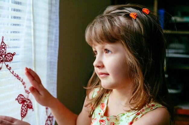 Sad little girl looking at window