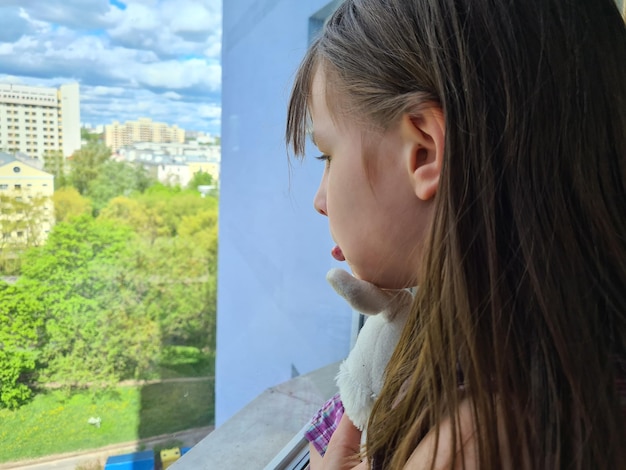 Sad little girl looks out window closeup