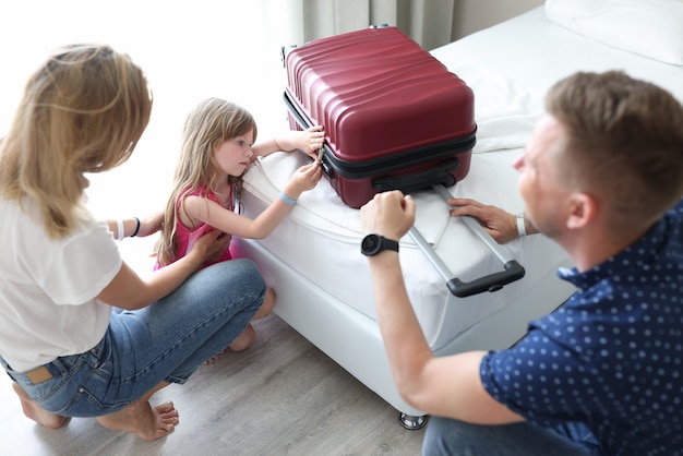 Photo sad little girl looks at suitcase sitting next to her parents