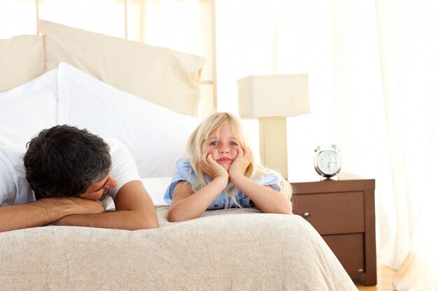 Sad little girl lying on bed with her father