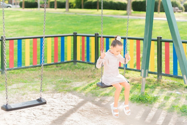 Sad little girl sitting alone on a swing looking down