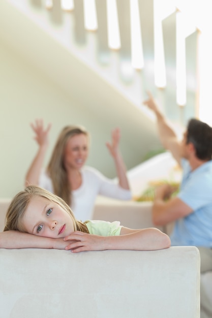 Sad little girl with fighting parents behind her