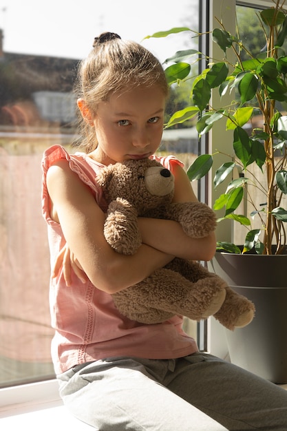 Sad little girl with her teddy bear at the window.