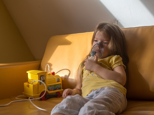 Photo sad little sick girl in pajamas makes inhalation sitting on the couchchild is ill
