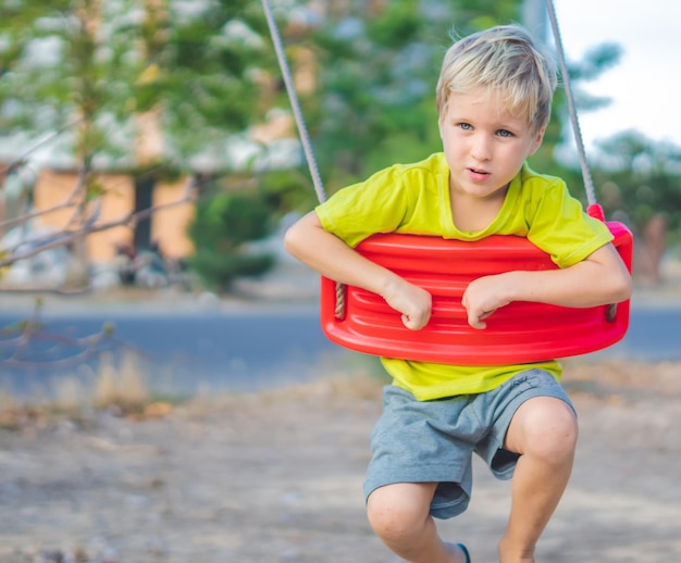 Sad lonely boy sitting on swing waiting for friends or while parents are busy Summer childhood leisure friendship and people concept