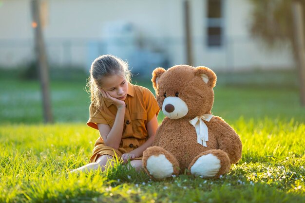 Sad lonely child girl spending time together with her teddy bear friend outdoors on sunny backyard loneliness at preteen age