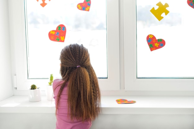 A sad lonely girl looks out the window decorated with heartshaped cards