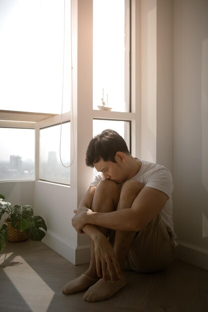 Sad and lonely man sits on the floor hugging his knee