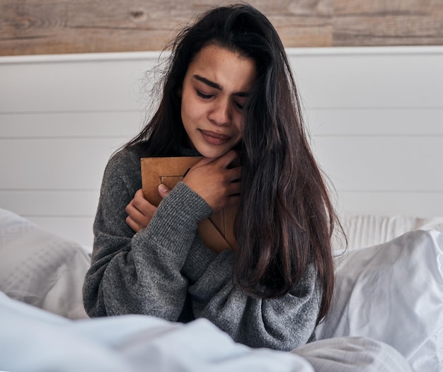 Sad loss and woman crying with a photo for memory while in bed in the morning Depression tears and girl with a picture frame in the bedroom during grief sadness and sorrow about death in a house