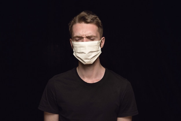 Sad man in protective mask on black background. Prevention against pneumonia, keep on being on quarantine, staying home. Chinese coronavirus treatment. Healthcare, medicine, isolation concept.