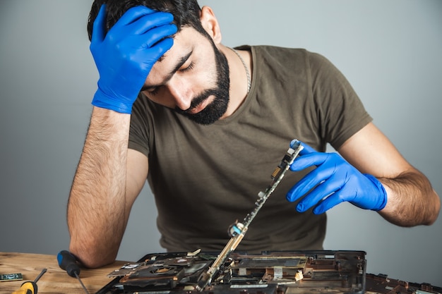 Foto uomo triste che ripara computer al tavolo